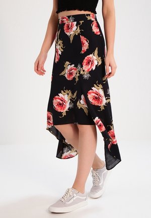 Zwarte bloemenrok met een hoge-lage zoom, voorzien van grote roze rozen en groene accenten. Gecombineerd met grijze sneakers. Gladde stoffen textuur.