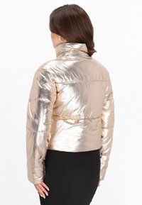 Gekürzte, metallisch goldene Pufferjacke mit Stehkragen, glänzender Textur und gesteppten Details an den Schultern und Seiten Nähten.
