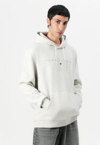 Lys grå hettegenser laget av fleece, med en frontlomme og snorhette. "TOMMY JEANS"-logo i blått over brystet.