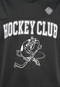 Μαύρη αθλητική φανέλα με λευκή επιγραφή «HOCKEY CLUB» και ένα καρτούν σκύλο που παίζει χόκεϊ κρατώντας ένα ραβδί και μια παγοκύστη κάτω από το κείμενο.