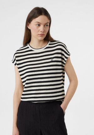 Striped short-sleeve top in black and cream knit, featuring a round neckline and a small logo on the left side. Paired with dark pants.