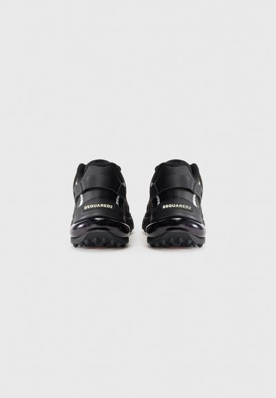O pereche de adidași negri Dsquared2, prezentați din spate, cu tălpi căptușite și logo-ul mărcii pe eticheta din călcâi, pe un fundal alb simplu.