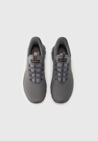 Zapatos deportivos grises con parte superior de tela de malla, cordones planos, puntera reforzada y logo de Skechers. La suela presenta un patrón texturizado para mayor agarre.