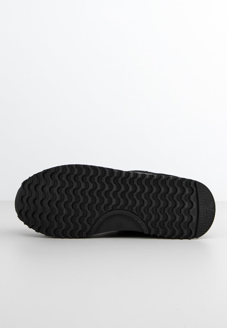 Suela de zapatilla negra con un patrón texturizado y ondulado. Material de goma duradera y surcos circulares para mayor agarre. Diseño simple sin adornos.