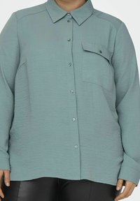 Světle modrá, texturovaná košile s límečkem a náprsní kapsou, se shodnými knoflíky a dlouhými rukávy.