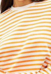 Gestreiftes Langarmshirt in Weiß und Orange mit Rundhalsausschnitt. Der Stoff wirkt glatt, mit horizontalen Streifen, die in der Breite variieren.