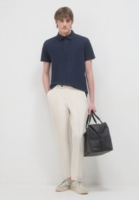 Polo shirt blu navy con colletto, pantaloni plissettati color crema, scarpe grigio chiaro e una borsa in pelle nera con design strutturato e doppi manici.