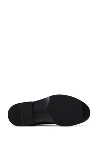 Suola di scarpa nera con modelli di grip testurizzati sul tallone e sulla parte anteriore, esposta su uno sfondo bianco.