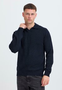Dunkelblauer Pullover mit V-Ausschnitt und Kragen, aus einem gestrickten Stoff gefertigt. Verfügt über lange Ärmel und gerippte Bündchen. Strukturiere Oberfläche.