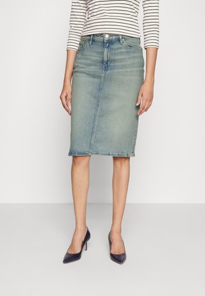 Kvinde iført en falmet blå denim knælængde nederdel, stribet langærmet skjorte og mørke spidse høje hæle.