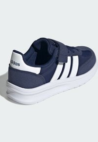 Chaussure de sport marine avec des rayures blanches et un logo. Équipée d'une sangle à boucle et d'une tige en tissu doux, conçue pour le confort et le soutien.