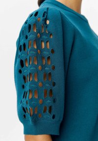 Tealfärgad tröja med stickade puffärmar som har utskärningar med geometriska mönster och ribbad manschett. Mjuk textur, rund halsringning.