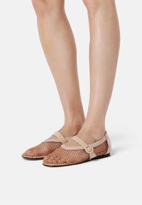 Brown mesh flats with a rounded toe and flat heel, accented by a beige strap with a circular buckle. Textured mesh material.