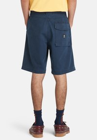 Pantaloni corti blu navy con una tasca posteriore caratterizzata da un logo. Realizzati in cotone, hanno una vestibilità comoda e orli risvoltati. Indossati con stivali e calzini.