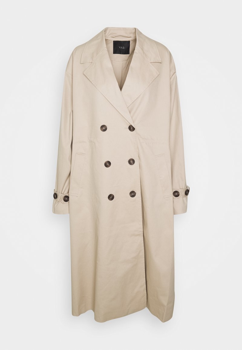Trench-coat long beige à double boutonnage avec larges revers, six boutons foncés et poignets boutonnés, suspendu sur un fond clair.
