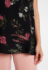 Černé tričko s květinovým vzorem v růžových a bílých květech, doplněné světle růžovými kalhotami. Hladká textura, krátké rukávy.