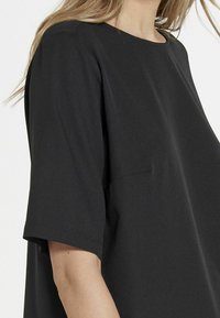 Top corto nero con maniche corte, dalla vestibilità grande, colletto rotondo e texture di tessuto morbida. I dettagli delle cuciture sulle spalle aggiungono una leggera struttura.
