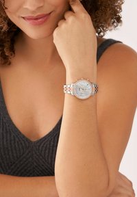 Zilveren en roségouden polshorloge met een ronde wijzerplaat, een gloeiend interieur, kristallen accenten en een gekoppelde metalen band.