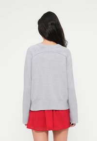 Pull en maille gris clair avec manches longues, poignets et ourlet côtelés. Un col rond et un léger motif texturé à l'arrière ajoutent du détail.