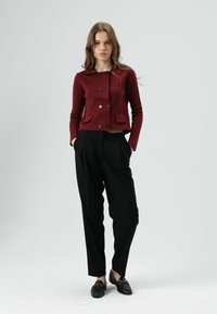 Veste courte bordeaux avec col, design croisé et deux poches avant, associée à un pantalon noir ample et des mocassins noirs.