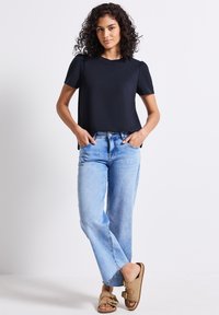 Haut noir à manches courtes avec un col rond, associé à un jean en denim bleu clair, ample et des sandales beiges avec des brides et des clous.