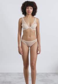 Μπέζ στηθόδεσμος με επένδυση και διαφάνειες, που διαθέτει φαρδιές τιράντες και αντίστοιχο διαφανές σλιπ. Λείο ύφασμα και μινιμαλιστικός σχεδιασμός.