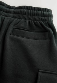 Pantalon de survêtement noir avec une finition texturée, doté d'une taille élastique et d'une petite poche plaquée au dos. Tissu lisse, design minimaliste.