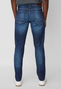 Jeans de mezclilla azul oscuro con un corte slim, que cuentan con dos bolsillos traseros, un ligero desvanecimiento y una etiqueta de cuero marrón en la cinturilla. Diseño clásico con dobladillo.