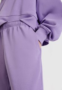 Lilla loungewear med en afslappet pasform top og bukser med elastisk talje, lavet af glat stof med manchetter og lomme detaljer.