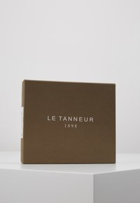 Brown rectangular box with a smooth texture, featuring the text "LE TANNEUR 1898" in white font on the front. Minimalistic design.