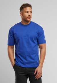 Blå bomulds T-shirt med korte ærmer, en rund halsudskæring og en glat tekstur. Har et lille logo i hvidt på venstre ærme.