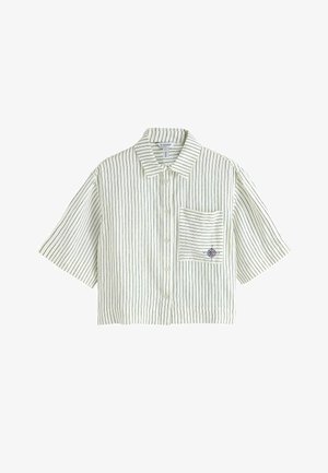 Cămașă albă, scurtă, cu mâneci scurte, dungă verticală subțire neagră, nasturi în față, guler și un buzunar cu un mic emblema de busolă.