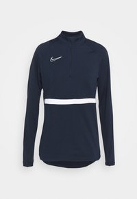 Tmavě modrý sportovní top s dlouhým rukávem, vysokým límcem, čtvrtinovým zipem, bílým vodorovným pruhem a logem Nike Swoosh na levé straně hrudi.