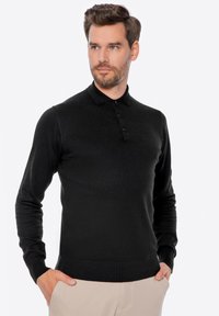 Schwarzes Langarm-Polohemd mit Kragen, ausgestattet mit einer Knopfleiste mit drei Knöpfen sowie gerippten Bündchen und Saum. Glatte Stoffstruktur.
