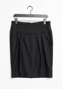 Musta kynähame, joka on tehty sileästä kankaasta ja siinä on jämäkkä vyötärö. Edessä laskokset ja helma laskeutuu polven yläpuolelle. Ripustettu koukkuun.