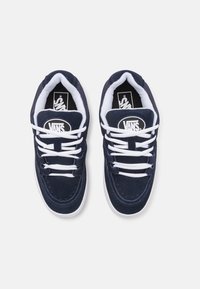 Navy modré semišové tenisky s bílými tkaničkami a gumovou podrážkou. Obsahují polstrovaný límec a logo Vans na jazyku. Klasický design s kulatou špičkou.