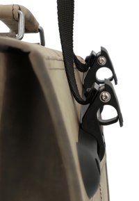 Bolsa de lona marrón con superficie texturizada, que cuenta con cierres de metal negro y una correa tejida. Vista en primer plano que resalta los detalles del hardware.