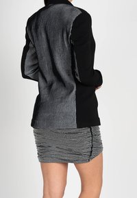 Blazer noir et blanc avec un motif rayé texturé dans le dos et un devant lisse, associé à une jupe froncée noire et blanche.