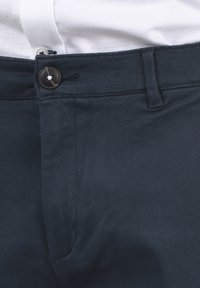 Chinos bleu marine avec fermeture à bouton, poches avant et texture lisse. La ceinture est cousue pour une durabilité accrue.