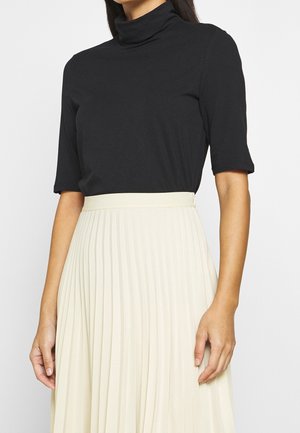 Musta, istuva poolkaelusega t-särk lühikeste varrukatega, millele on sobitatud kortsuline beež seelik. Sile tekstuur, lihtne disain, ilma nähtavate mustrite või riistade detailideta.