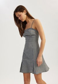 Schwarz-weißer karierten Kleid mit tailliertem Oberteil, dünnen verstellbaren Trägern und ausgestelltem Rock, der über ein gerafftes Dekolleté-Detail und eine glatte Textur verfügt.