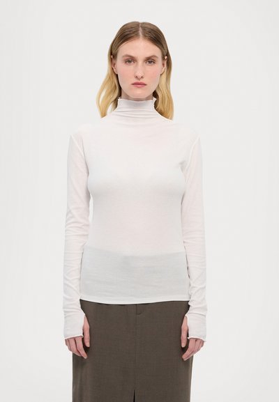 Vit långärmad polotröja i lätt, slät tyg. Har en figurnära design och förlängda ärmslut, som kombineras med en brun kjol.