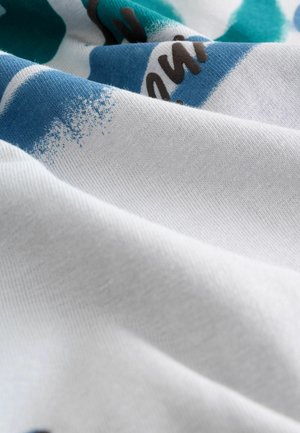 Bavlněná látka vystavená na bílém podkladu, s abstraktními modrými a černými vzory. Textura se zdá být jemná a hladká, s viditelnými tkaninami.