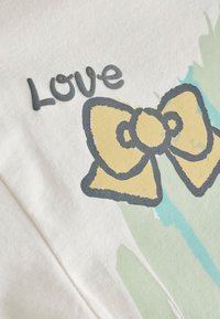Handwritten word "Love" next to a simple yellow bow with black outline on a white fabric background with pastel green and blue brush strokes.
