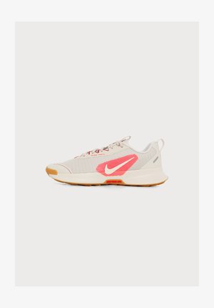 Chaussure de trail running Nike beige clair avec logo rose et blanc, semelle en gomme et lacets gris sur fond blanc.