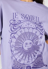 Light purple t-shirt featuring a sun graphic with astrological symbols, intricate line designs, and a soft, smooth texture.