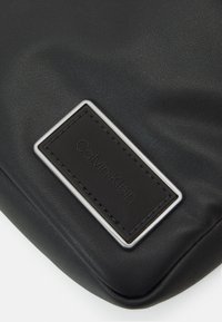 Borsa in pelle nera con finitura texturizzata, accessori in metallo rettangolari argentati e un'etichetta in tessuto nera embossata con "Calvin Klein."