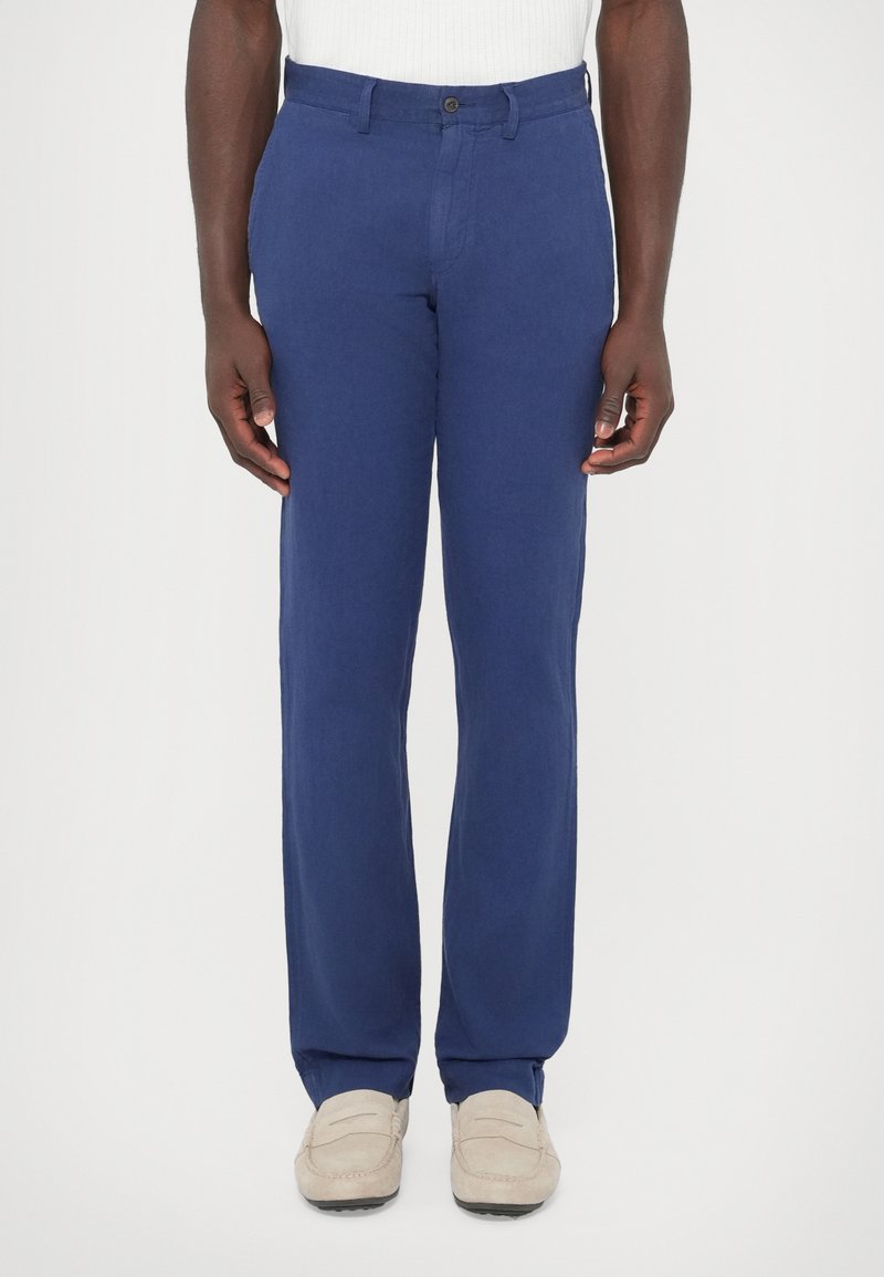 Kék len nadrág egyenes szabással, egy gombos záródással és övhurkokkal. Világos színű mokaszinokkal viselve.