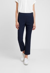 Námořnické modré, zúžené kalhoty z texturované tkaniny s jemným kostkovaným vzorem, kombinované s bílými teniskami a bílou košilí s krátkým rukávem.