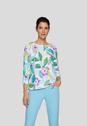 Leichte, langärmlige Bluse mit einem lebendigen Blumen- und Blattmuster in Lila, Grün und Türkis auf einem weißen Hintergrund; runder Halsausschnitt.